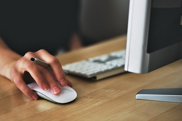 person holding a pen and using a computer mouse at the same time